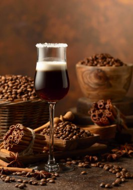 Kahverengi arka planda kremalı kahve likörü. Kahve çekirdekleri, tarçın çubukları ve anason masaya saçılmış..