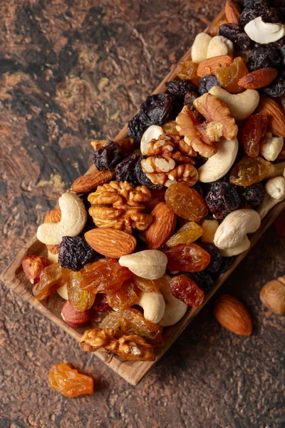 Mix of nuts and raisins on a brown rustic background. Presented raisins, walnuts, hazelnuts, cashews, pecans, and almonds. Top view.