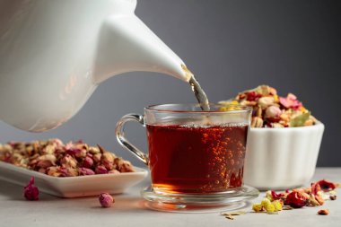 Bitki çayı bardağa dökülür. Kurumuş otlar ve çiçekler taş masaya saçılmış..