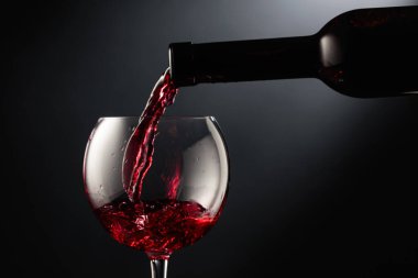 Kırmızı şarabı siyah arka planda bir şarap bardağına döküyorum..