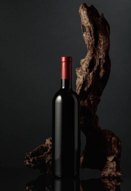 Siyah yansıtıcı arka planda bir şişe kırmızı şarap. Arka planda eski yıpranmış bir pürüz var. Metnin için alanı olan ön görünüm.