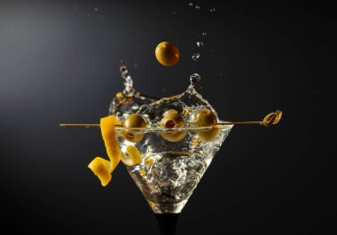 Siyah arka planda yeşil zeytinli ve limon kabuklu klasik sek martini kokteyli. Sıçratmalı martini. Metnin için boş yer.