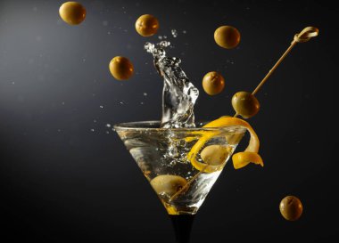 Siyah arka planda yeşil zeytinli ve limon kabuklu klasik sek martini kokteyli. Sıçratmalı martini. Metnin için boş yer.