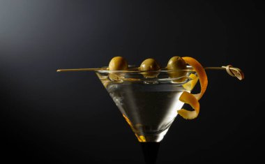 Siyah arka planda yeşil zeytinli ve limon kabuklu klasik sek martini kokteyli. Metnin için boş yer.