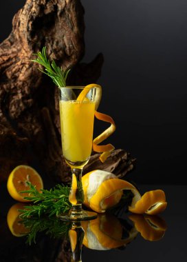 Siyah yansıtıcı arka planda geleneksel İtalyan likörü Limoncello. Bir bardak limon likörü ve arka planda biberiye dalı..