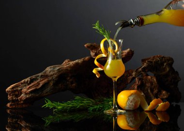 Siyah yansıtıcı arka planda geleneksel İtalyan likörü Limoncello. Bir bardak limon likörü ve arka planda biberiye dalı. İçki bardağa dökülür..