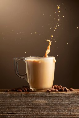 Bir bardak kahve, sütlü kahve ya da kahverengi arkaplanda su sıçramış kahve. Kahve fincanı ve kavrulmuş kahve çekirdekleri eski bir tahtanın üzerinde..