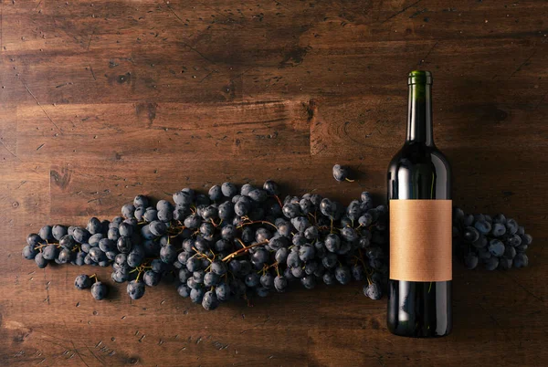 Blue grapes and bottle of red wine on an old wooden table. On a bottle old empty label. Copy space.