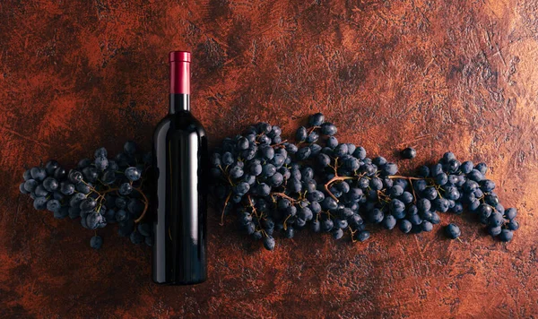 Kahverengi bir arka planda mavi üzüm ve bir şişe kırmızı şarap. Boşluğu kopyala.