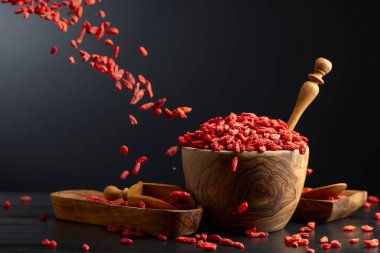 Siyah arka planda ahşap kasede kurutulmuş kurt üzümü. Çilekler hareket halinde.