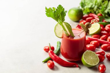 Salatalık, zeytin, limon ve kereviz ile süslenmiş Bloody Mary kokteyli. Beyaz taş bir masanın üzerinde malzemelerle domates suyu..