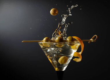 Siyah arka planda yeşil zeytinli ve limon kabuklu klasik sek martini kokteyli. Sıçratmalı martini. Metnin için boş yer.