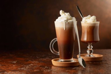 Kremalı sütlü çikolatalı içecekler. Eski kahverengi bir masada krem şantili ev yapımı latte. Boşluğu kopyala.