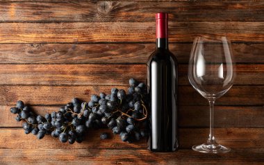 Eski ahşap bir masada mavi üzümler ve bir şişe kırmızı şarap. Boşluğu kopyala.