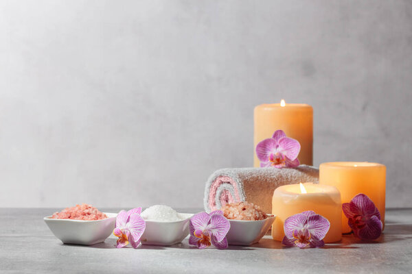 Sea salt, towels, orchid flowers, and burning candles on a grey background. Spa concept with copy space.