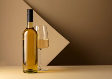 Bottle and glass of white wine on a beige background. Copy space.