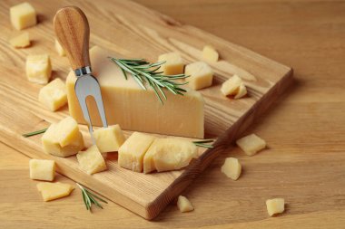 Parmesan cheese with rosemary and fork on a wooden cutting board.