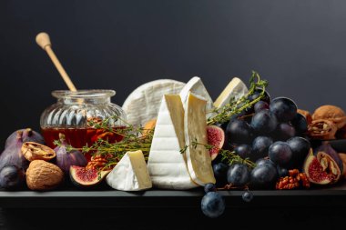İncirli, üzümlü, kekik, ceviz ve ballı Camembert peyniri. Siyah arka planda meyveli yumuşak peynir..