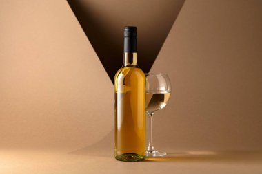 Bottle and glass of white wine on a beige background. Copy space.