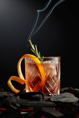Buzlu, portakal kabuklu ve biberiyeli eski moda kokteyl. Karanlık bir arka planda yanan bir biberiye dalı olan viski..