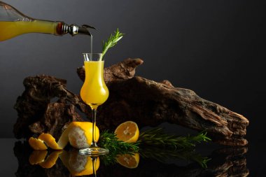 Siyah yansıtıcı arka planda geleneksel İtalyan likörü Limoncello. Bir bardak limon likörü ve arka planda biberiye dalı. İçki bardağa dökülür..