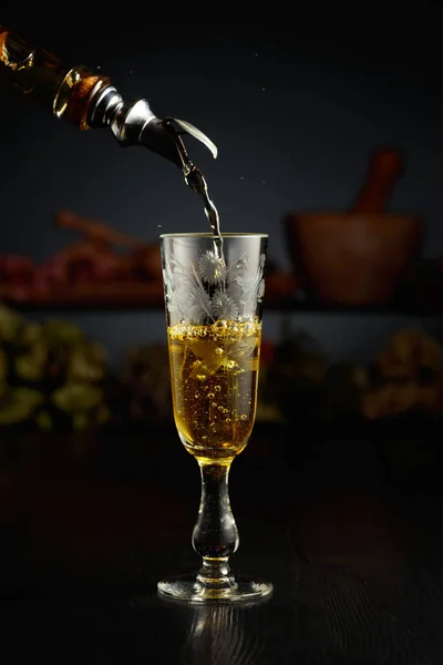 ヴィンテージボトルからグラスに黄色いハーブ酒を注ぎます バックグラウンドで乾燥ハーブと古い台所用品 — ストック写真