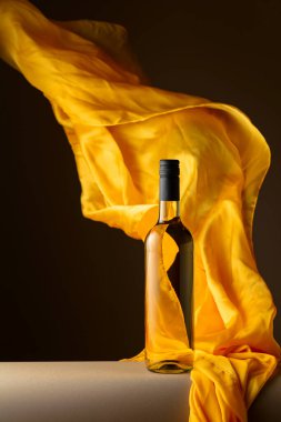 Bir şişe beyaz şarap ve koyu bir arka planda çırpınan sarı kumaş..