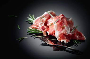 Italian prosciutto or Spanish jamon with rosemary on a black background. Copy space.