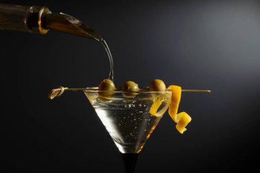 Siyah arka planda yeşil zeytinli ve limon kabuklu klasik sek martini kokteyli. Metnin için boş yer.