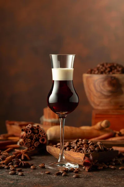 Coffee liquor with cream on a brown background. Coffee beans, cinnamon sticks, and anise are scattered on the table.