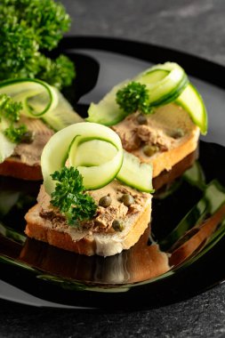 Pate, taze salatalık, kapari ve maydanozlu sandviç. Siyah tabakta ezmeli tost..