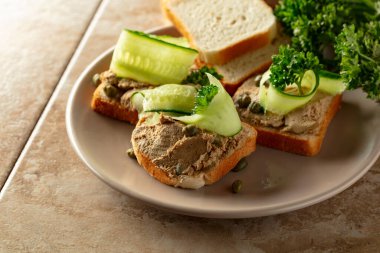 Bej tabakta ezmeli tost. Pate, taze salatalık, kapari ve maydanozlu sandviç..