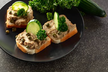 Pate, taze salatalık, kapari ve maydanozlu sandviç. Siyah tabakta ezmeli tost..