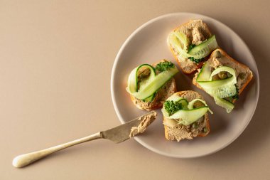 Pate, taze salatalık, kapari ve maydanozlu sandviç. Bej arka planda ezmeli tost. Üst görünüm, alanı kopyala.