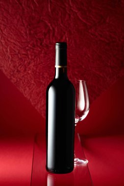Bottle of red wine and an empty wine glass on a red background.