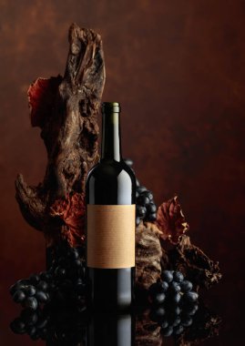 Eski etiketli bir şişe kırmızı şarap. Arka planda eski yıpranmış çıkıntı ve mavi üzümler. Boşluğu kopyala.