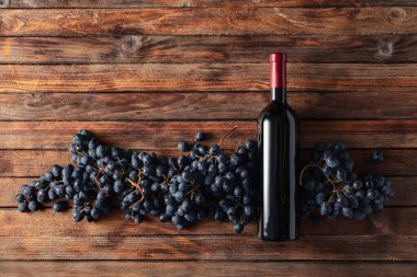 Eski ahşap bir masada mavi üzümler ve bir şişe kırmızı şarap. Boşluğu kopyala.
