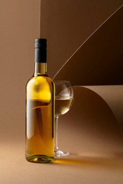 Bottle and glass of white wine on a beige background. Copy space.