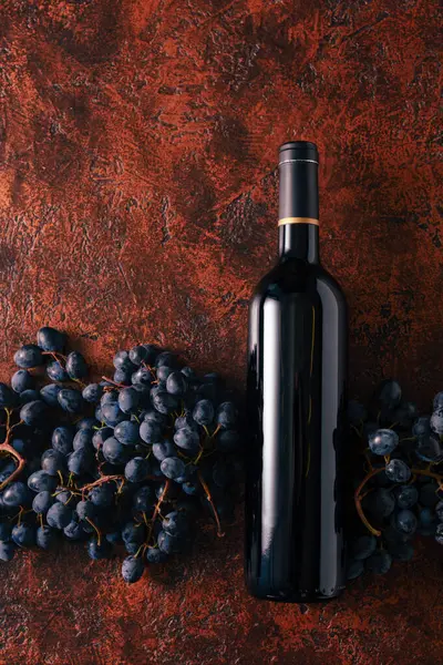 Blue grapes and bottle of red wine on a brown vintage background. Copy space.