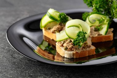 Pate, taze salatalık, kapari ve maydanozlu sandviç. Siyah tabakta ezmeli tost..