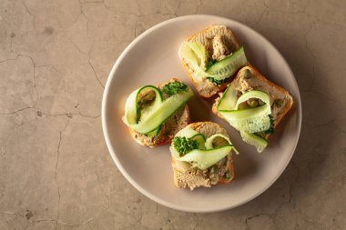 Pate, taze salatalık, kapari ve maydanozlu sandviç. Bej taşlı arka planda ezmeli tost. Üst görünüm, alanı kopyala.