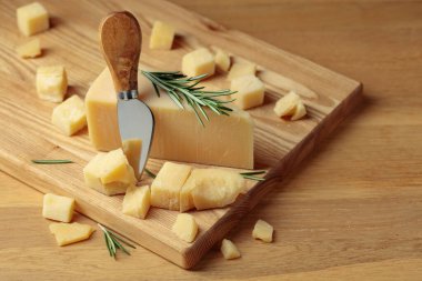 Parmesan cheese with rosemary and fork on a wooden cutting board.
