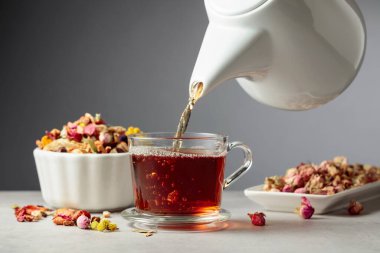 Bitki çayı bardağa dökülür. Kurumuş otlar ve çiçekler taş masaya saçılmış..