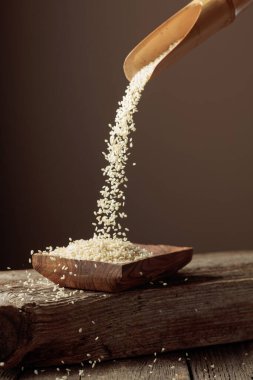 Tahta tabakta tahtadan bir kaşıkla beyaz susam taneleri dökülüyor. Boşluğu kopyala.