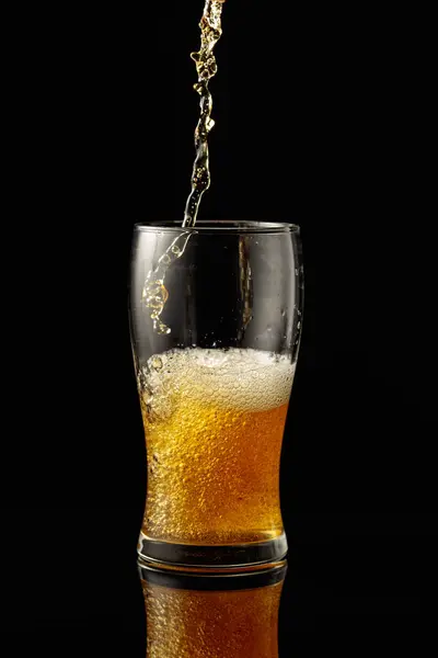 Pouring beer into a glass. Glass of beer on a black reflective background.