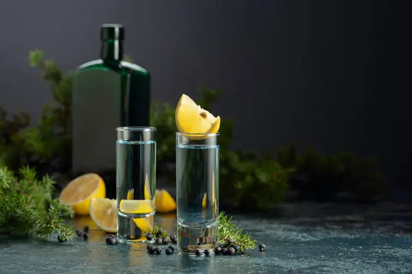 Blue gin and juniper branches on an old dark blue table. Gin with juniper berries, lemon slices, and vintage bottle.