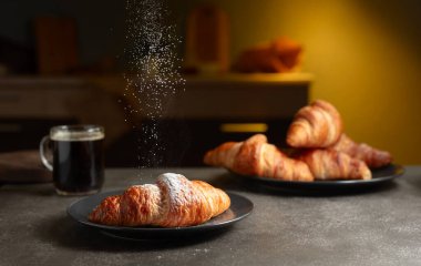 Taze kruvasan ve mutfak masasında sade kahve. Şeker tozu serpiştirilmiş kruvasanlar. Seçici odak.