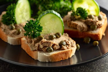 Pate, taze salatalık, kapari ve maydanozlu sandviç. Siyah tabakta ezmeli tost..
