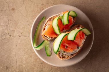 Tütsülenmiş alabalık, krem peynir, taze salatalık ve taş bir masada kapari. Üst görünüm, alanı kopyala.