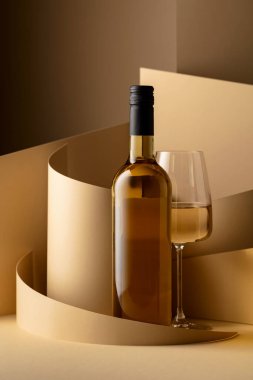 Bottle and glass of white wine on a beige background. Copy space.
